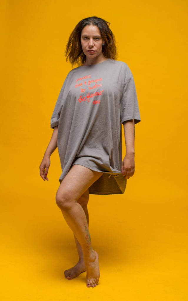 A long, flowing, grey 5XL T-Shirt with a neon-orange print saying "Please don't forget to water the flowers, Xoxo!", worn by a female model in front of a yellow background.